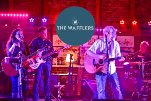 The Wafflers - An image of the band performing on stage with moody red lighting.